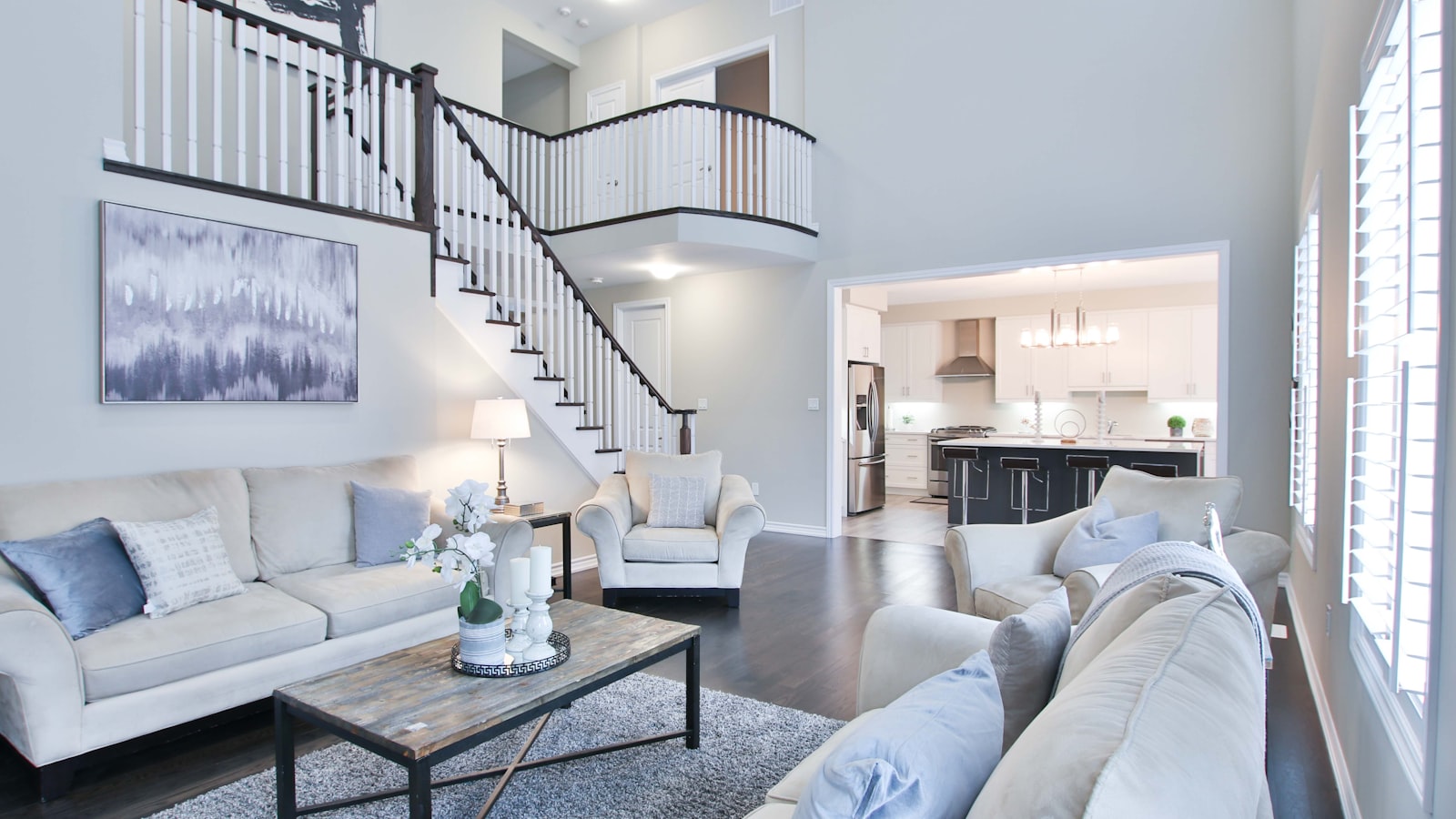 Open-plan two-story living room with a curved staircase and a white modern kitchen visible in the background