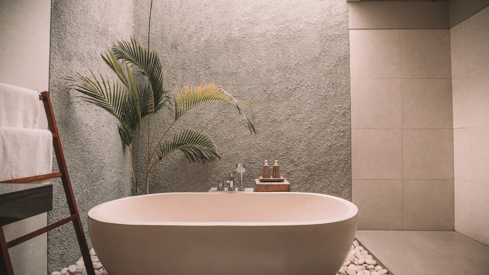 Spa-style master bathroom with a freestanding soaking tub, textured stucco wall, and tropical palm accent