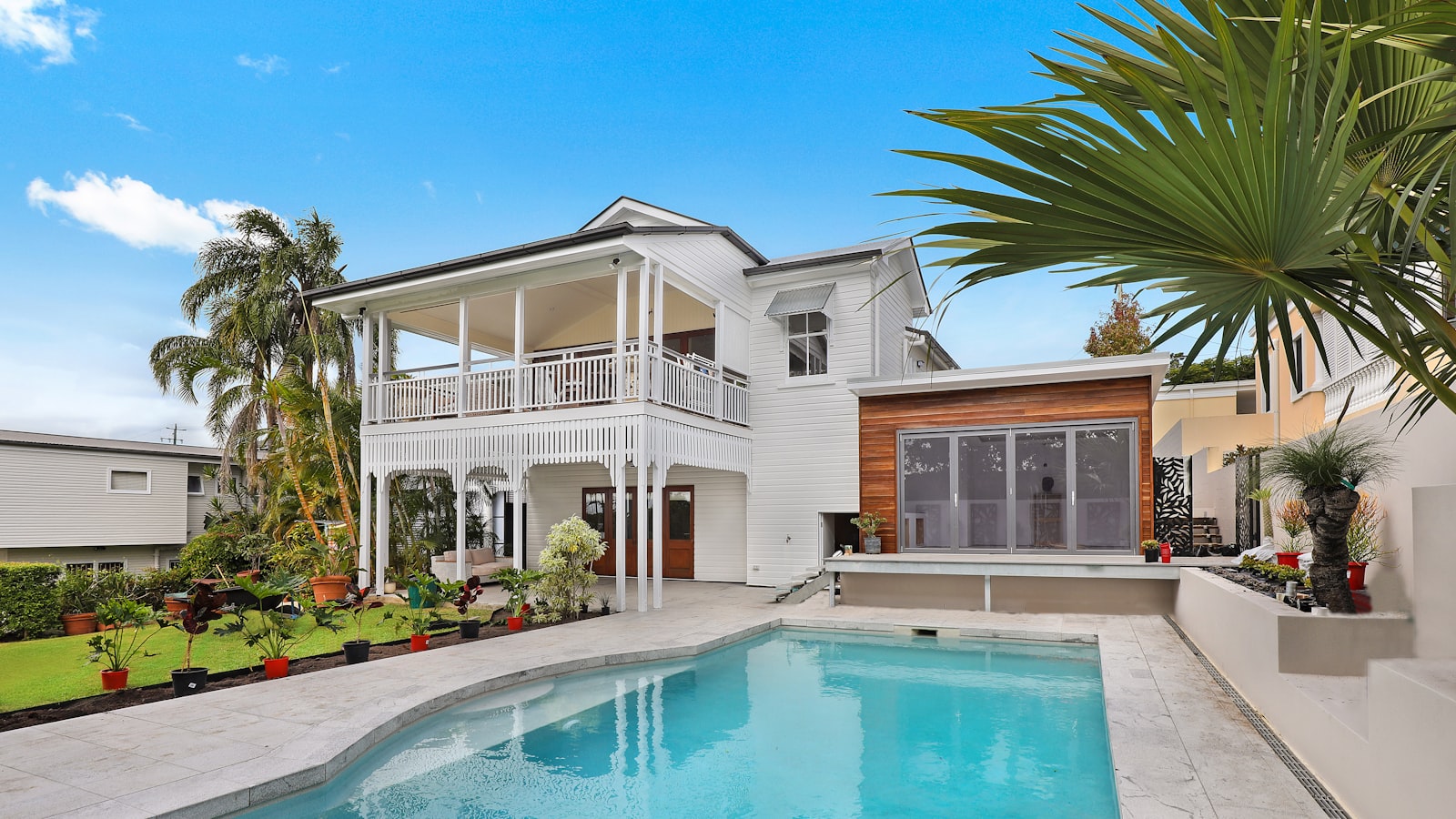 Two-story white coastal home with a second-floor balcony, palm trees, and a turquoise swimming pool