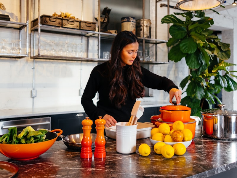 Homeowner preparing food on a dark marble kitchen counter with open shelving and modern cookware