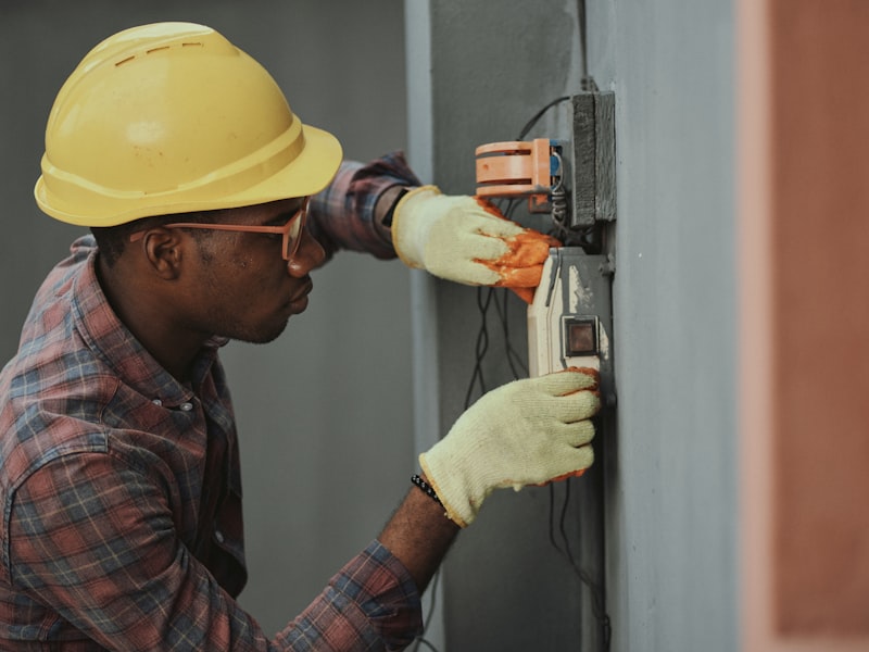 Contractor in yellow hard hat and safety glasses installing a wall-mounted utility panel